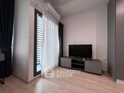 Modern living room with sleek TV setup and balcony access, featuring elegant curtains and wooden flooring.