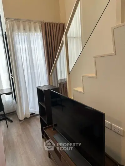 Modern living room with stylish staircase and large TV, featuring elegant curtains and wooden flooring.