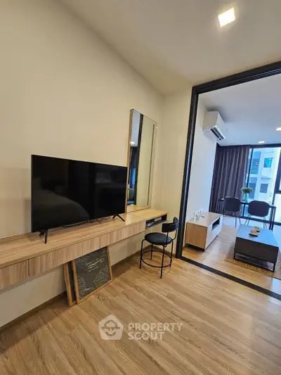 Modern living room with sleek TV setup and open layout leading to a stylish seating area.