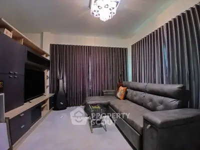 Modern living room with sleek gray sofa and entertainment center, featuring elegant curtains and ambient lighting.