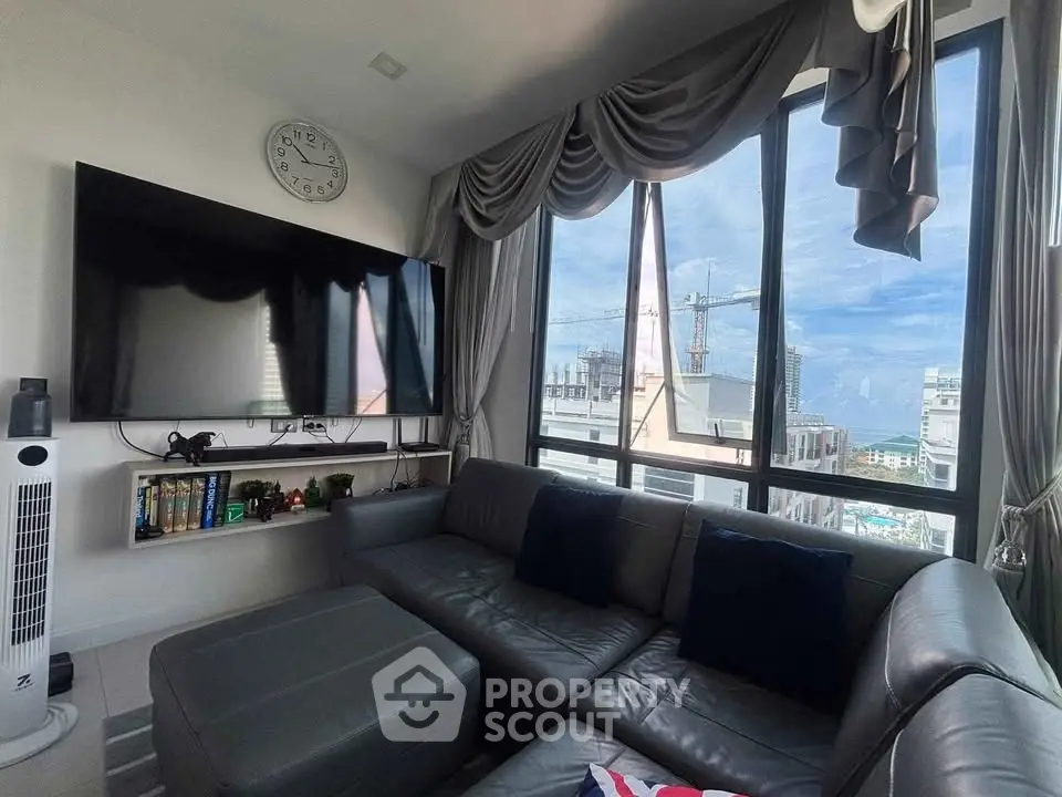 Modern living room with large windows offering a stunning city view, featuring a sleek leather sofa and wall-mounted TV.