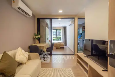 Modern living room with open layout, cozy seating, and view into bedroom and kitchen.