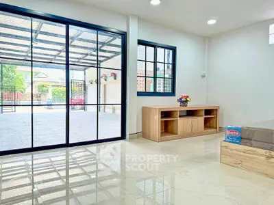 Spacious living room with large glass doors opening to a patio, featuring sleek tile flooring and modern decor.
