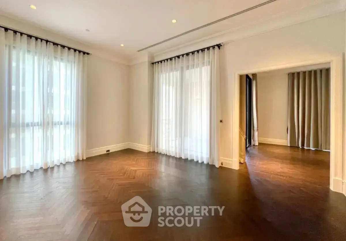 Spacious living room with elegant hardwood floors and large windows with sheer curtains.