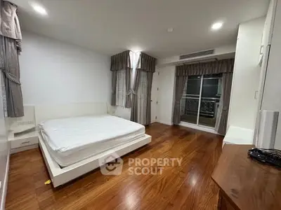 Spacious bedroom with wooden flooring and large windows in modern apartment.