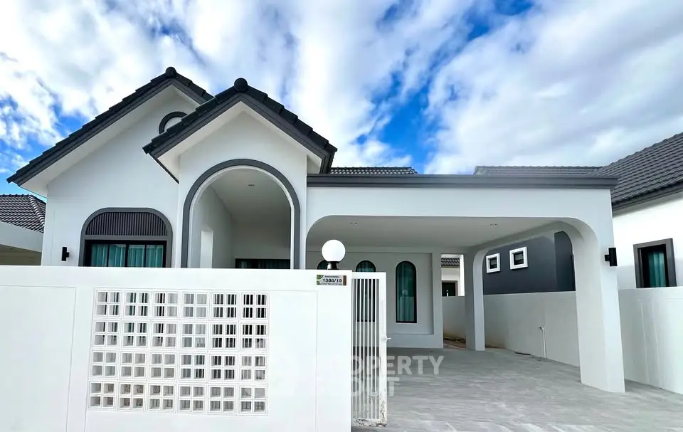 Modern white house with arched windows and spacious driveway under a blue sky.