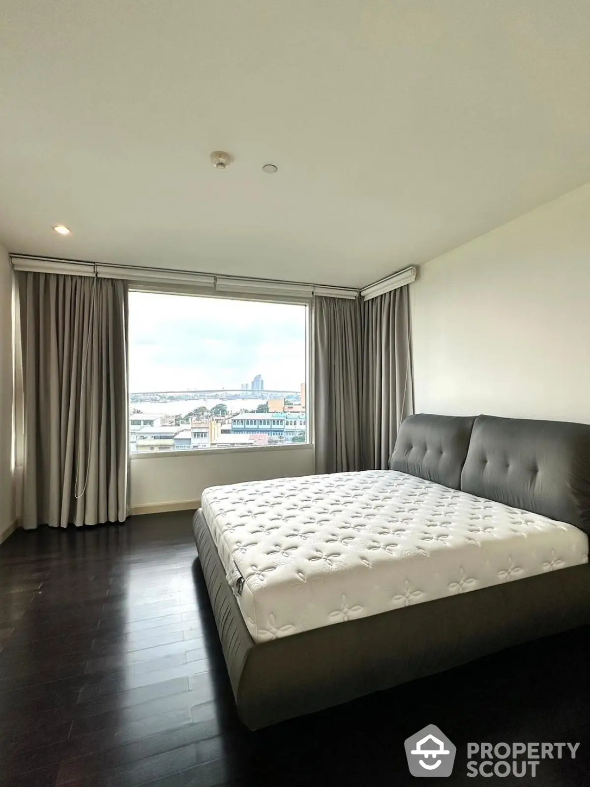 Spacious bedroom with large window offering stunning city view and elegant dark wood flooring.