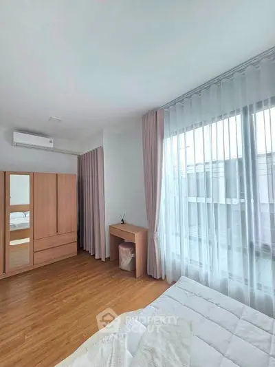 Bright bedroom with large window, wooden flooring, and modern furniture in a stylish apartment.