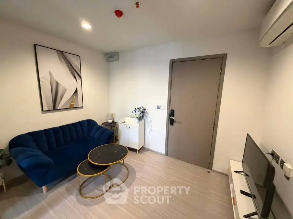 Modern living room with stylish blue sofa, chic coffee tables, and wall art in a cozy apartment.