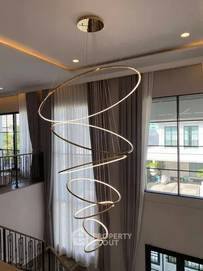 Elegant spiral chandelier in modern high-ceiling living room with large windows and natural light.