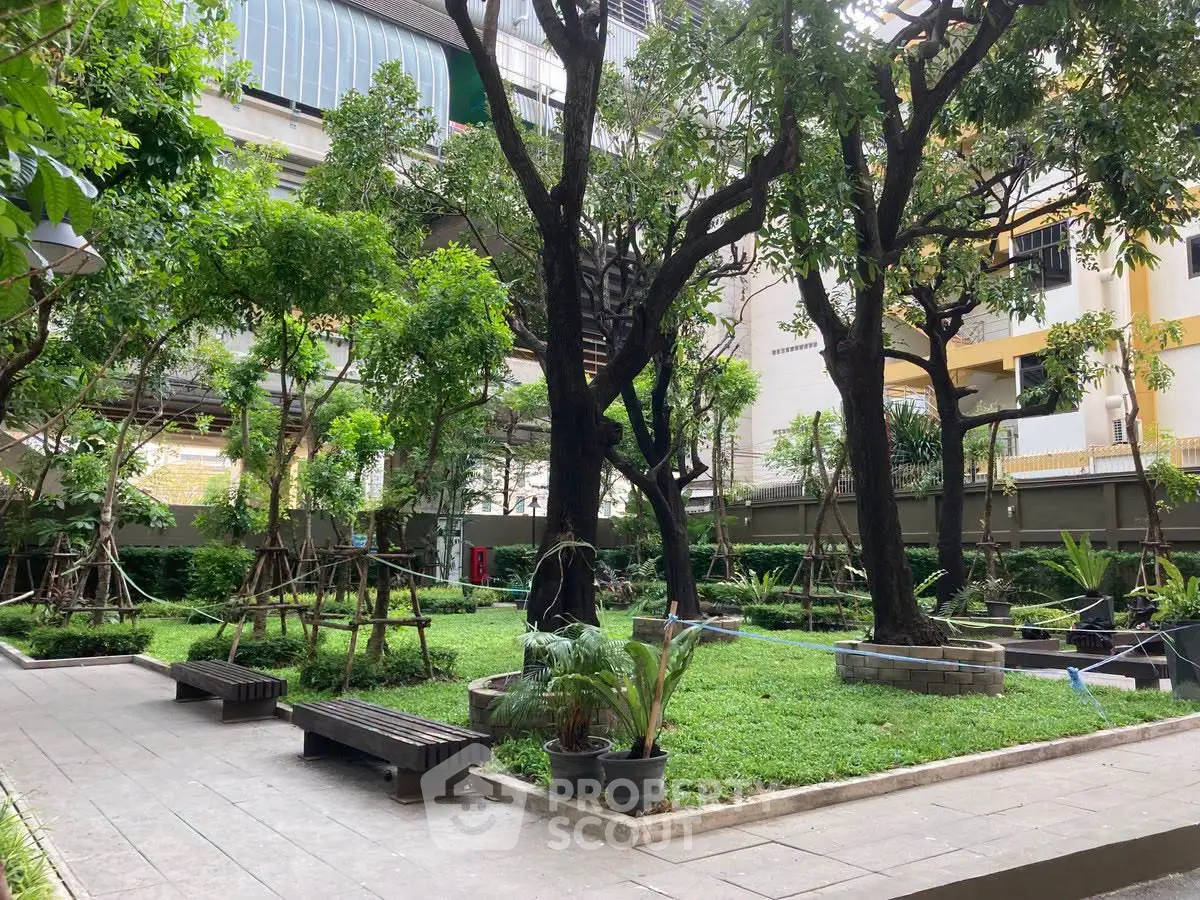Lush green garden area in a modern residential complex with mature trees and seating.