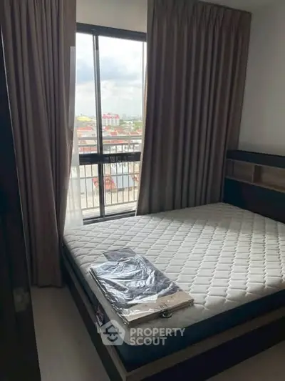 Cozy bedroom with large window offering city views, featuring a comfortable mattress and elegant curtains.
