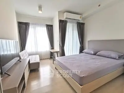 Modern bedroom with natural light, featuring a cozy bed, stylish curtains, and a sleek TV setup.