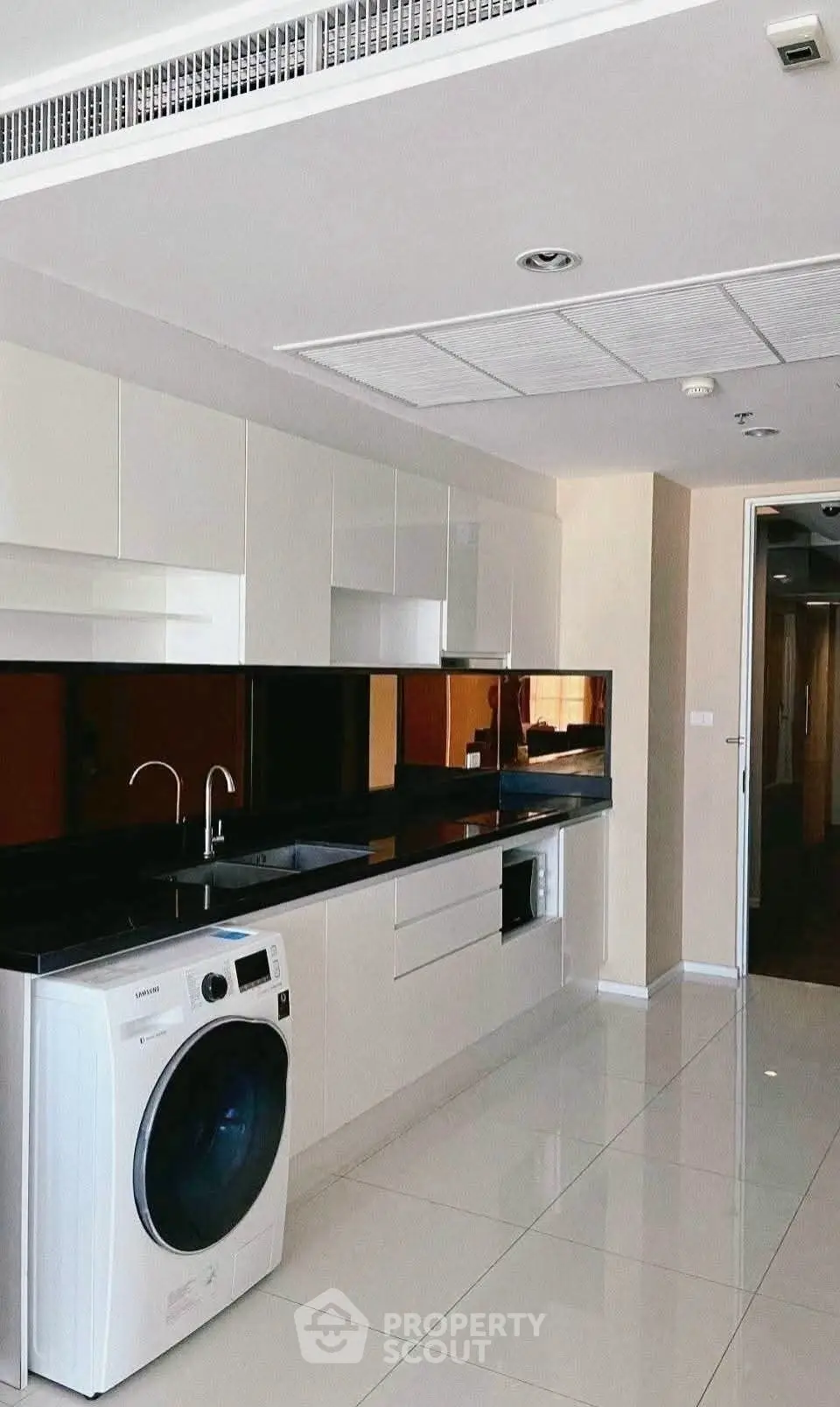 Modern kitchen with sleek cabinetry and built-in appliances, featuring a washing machine and glossy black countertops.