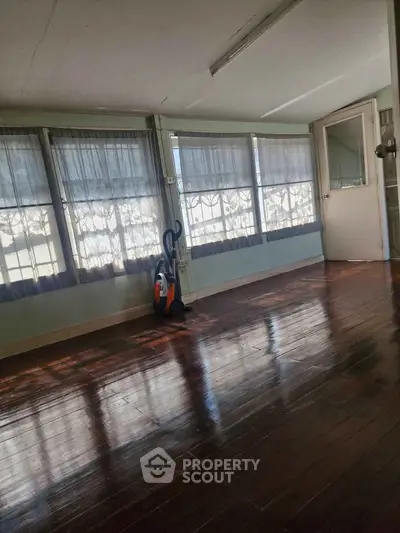Spacious sunlit room with polished wooden floors and large windows, perfect for a cozy living area.