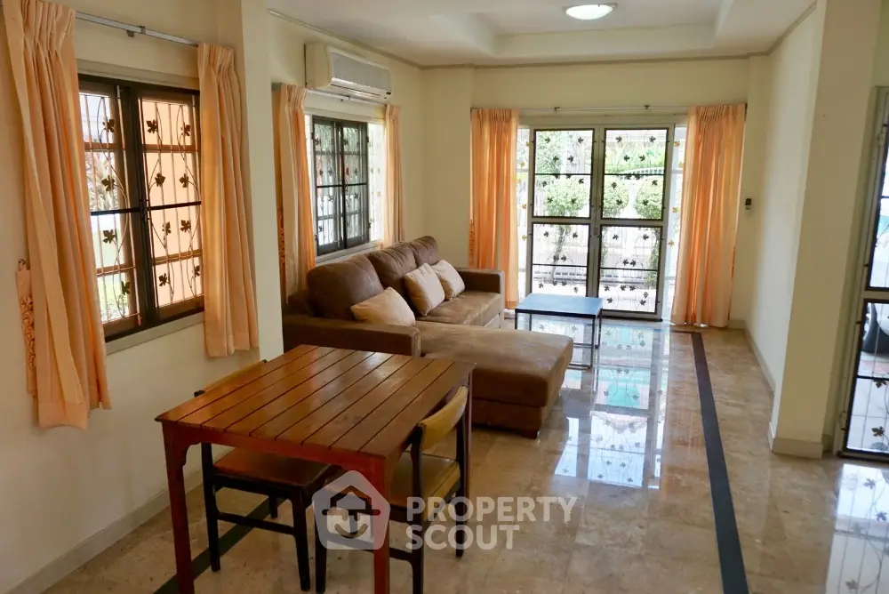 Spacious living room with polished tile flooring, large windows draped with orange curtains, and comfortable seating area leading to a sunny balcony.