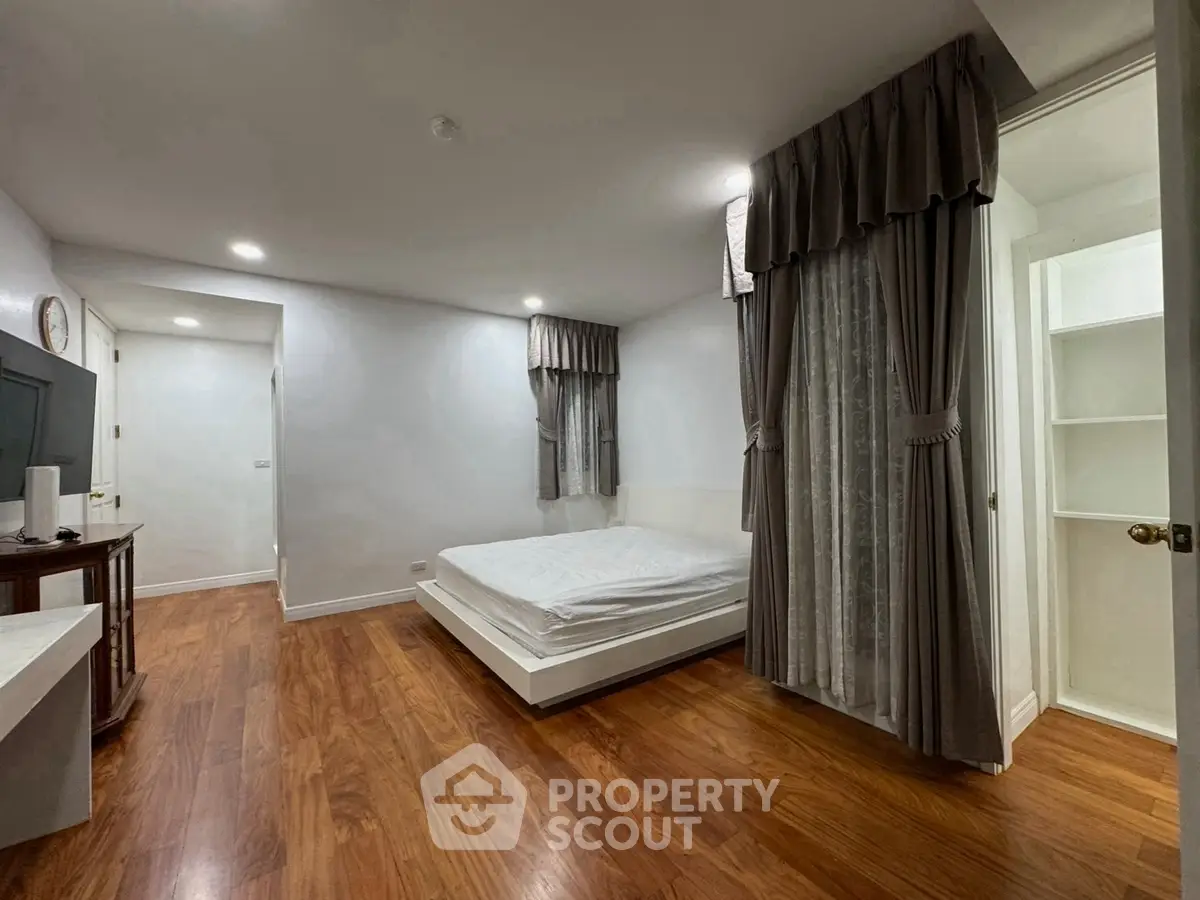Spacious bedroom with wooden flooring and elegant curtains in modern apartment.