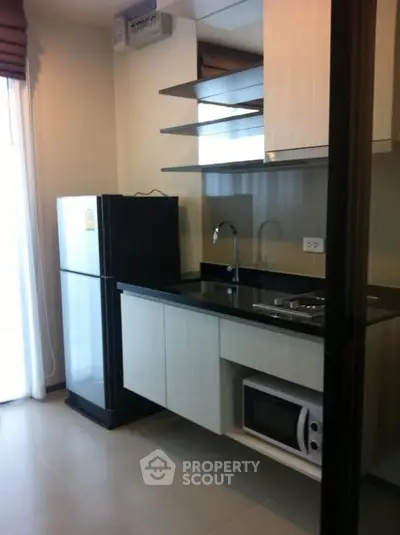 Modern kitchen with sleek cabinets, fridge, and microwave in a compact layout.