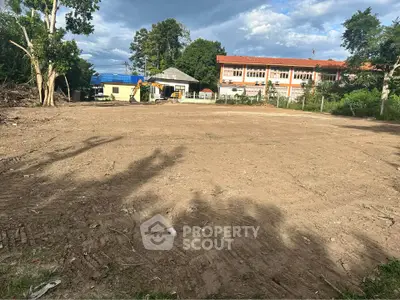 Spacious land plot with potential for development, surrounded by greenery and nearby buildings.