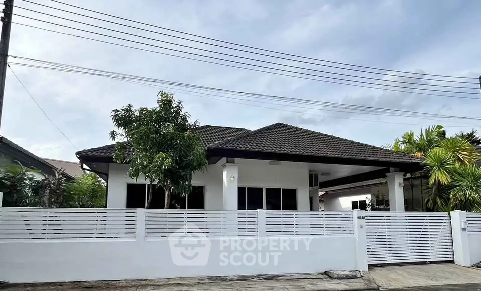 Charming single-story house with modern fence and lush greenery in a serene neighborhood.