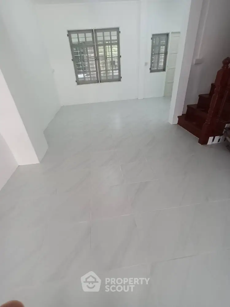 Spacious empty room with tiled flooring and staircase, ideal for customization.