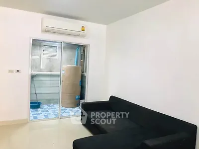 Modern living room with sleek black sofa and air conditioning, featuring a unique utility area view.