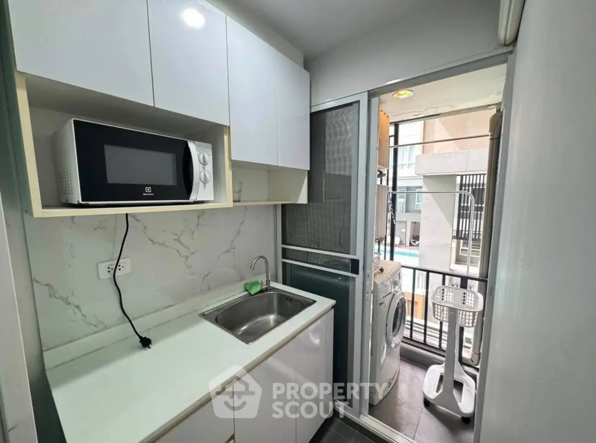 Compact kitchen with microwave and washing machine on balcony in modern apartment.