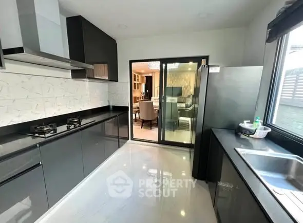 Modern kitchen with sleek black cabinetry and gas stove, featuring open view to dining area.
