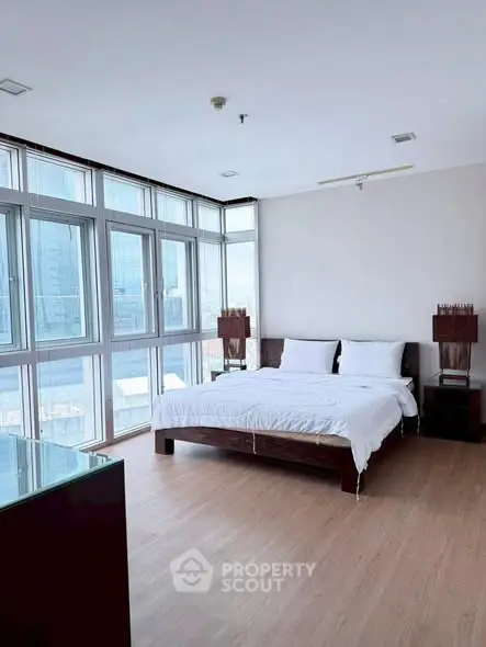 Spacious bedroom with large windows and modern decor in a high-rise apartment.
