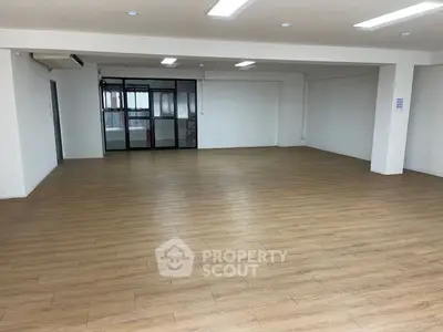 Spacious open-plan room with wooden flooring and glass partition, ideal for versatile use.