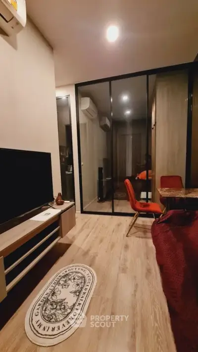 Modern living room with stylish decor and glass partition, featuring a cozy seating area and sleek TV setup.