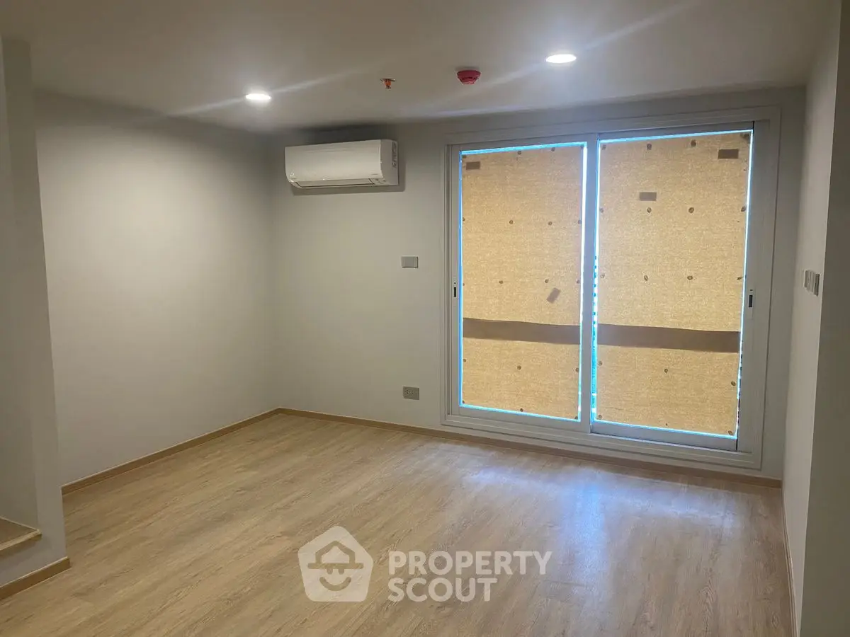 Spacious empty room with wooden flooring and large window, ideal for customization.
