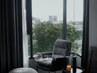 Cozy reading nook with plush chair and city view through large windows.