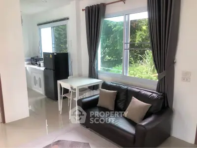 Modern living room with garden view, sleek black sofa, and adjacent kitchen area.