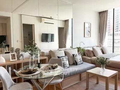 Modern open-plan living room with dining area and cozy bedroom, featuring stylish decor and large windows.