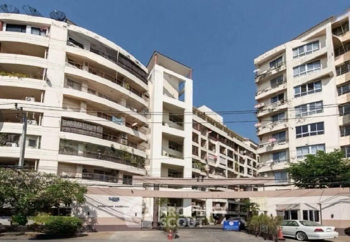 Modern multi-story apartment building with balconies and parking area in urban setting.