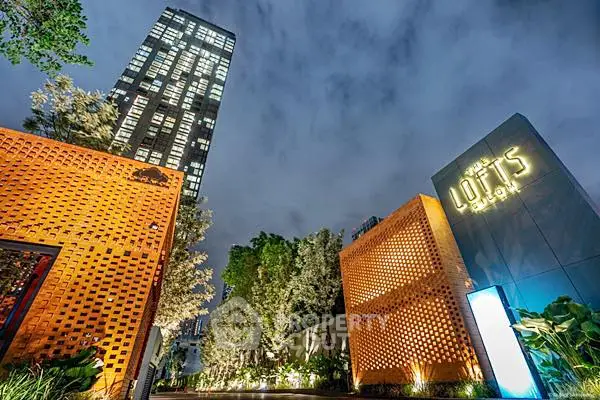 Stunning night view of modern high-rise building with illuminated entrance and lush greenery.