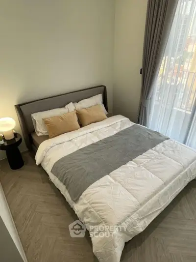 Cozy bedroom with modern decor and large window offering natural light.