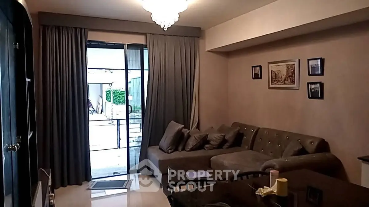 Cozy living room with elegant chandelier and plush sectional sofa, leading to a bright balcony.