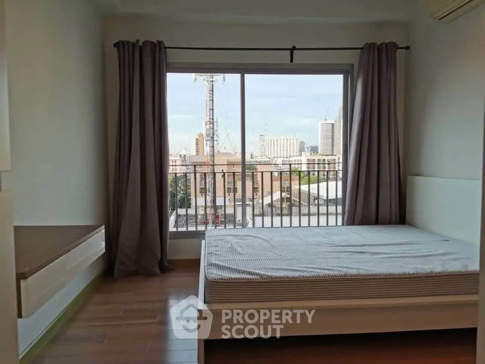 Modern bedroom with large window offering city view, featuring wooden flooring and minimalist design.