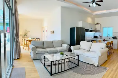 Spacious open-plan living room with modern kitchen and dining area, featuring cozy sofas and natural light.