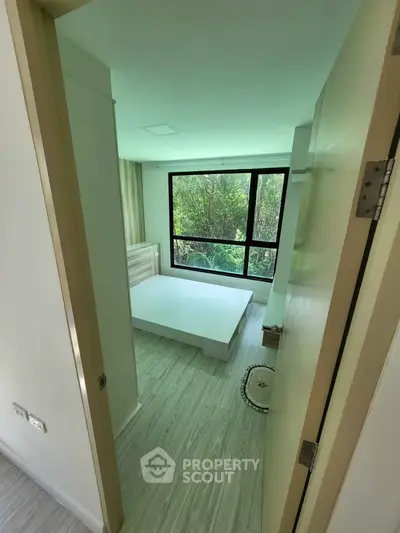 Modern bedroom with large window and minimalist design overlooking lush greenery.
