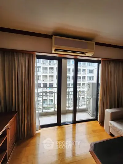 Spacious living room with balcony and city view, featuring wooden flooring and air conditioning.
