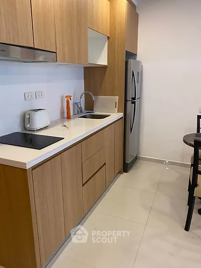 Modern kitchen with sleek wooden cabinets, stainless steel fridge, and electric cooktop in a compact layout.
