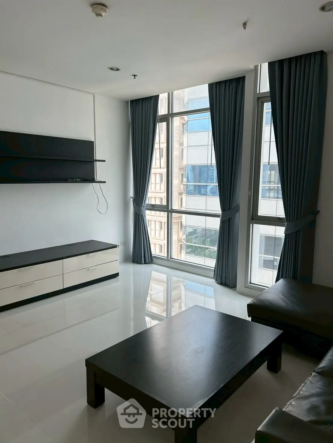 Spacious living room with large windows and modern furniture in a high-rise apartment.
