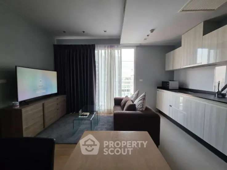 Modern living room with sleek kitchen, large TV, and cozy sofa in open layout apartment.