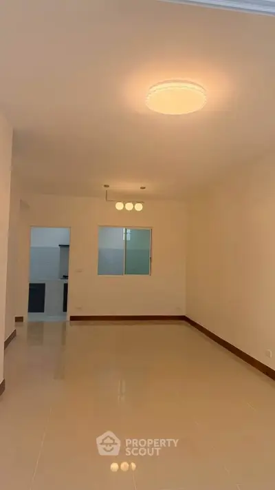 Spacious living room with modern lighting and tiled flooring, adjacent to a kitchen area.