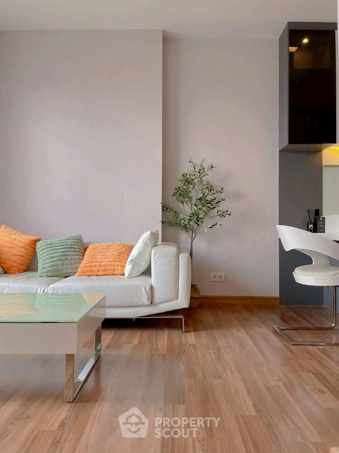 Modern living room with stylish decor and wooden flooring, featuring a sleek white sofa and vibrant cushions.