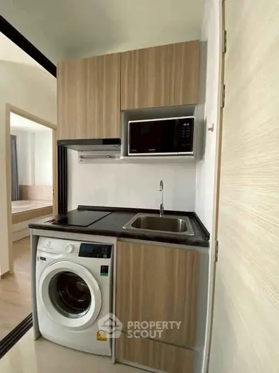 Compact modern kitchen with washing machine and microwave in stylish apartment.