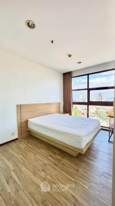 Bright bedroom with large window and city view, featuring a minimalist design and wooden flooring.